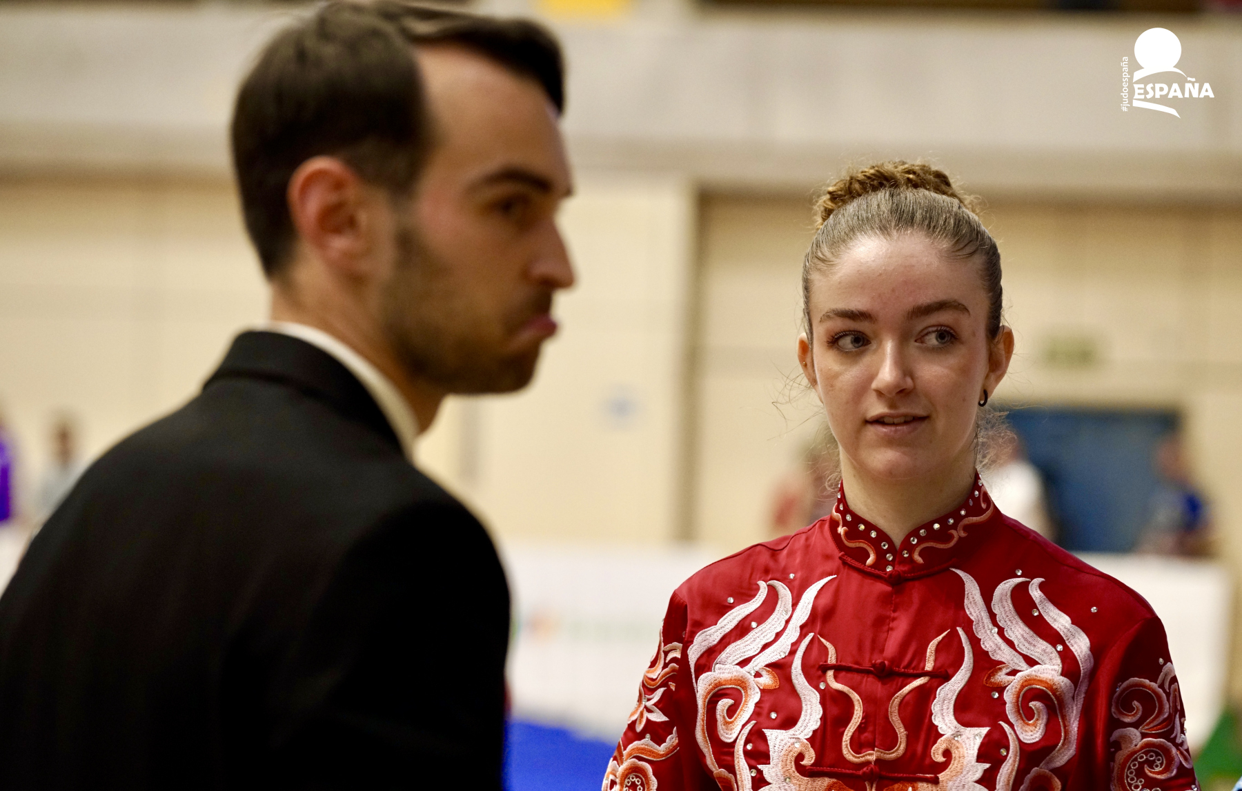 Competidor de Wushu con uniforme rojo bordado siendo evaluado por un juez durante un campeonato nacional en España