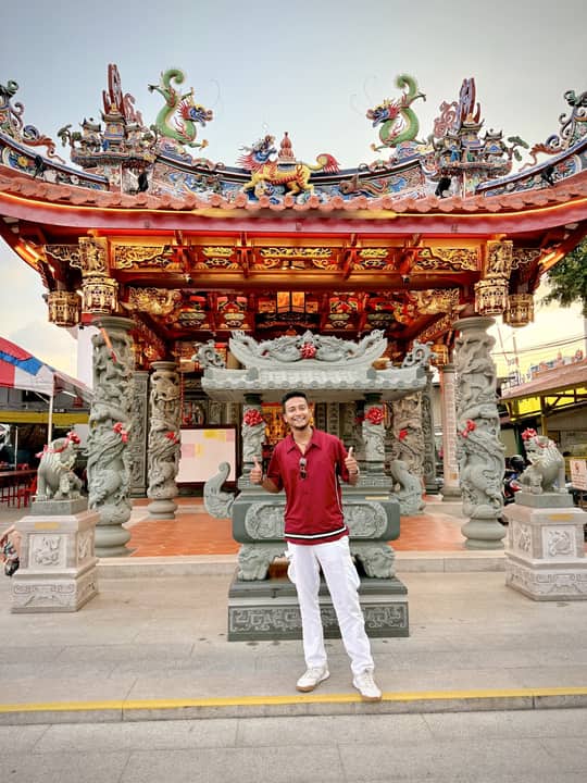 Before an ornate temple gate, Malaysia.