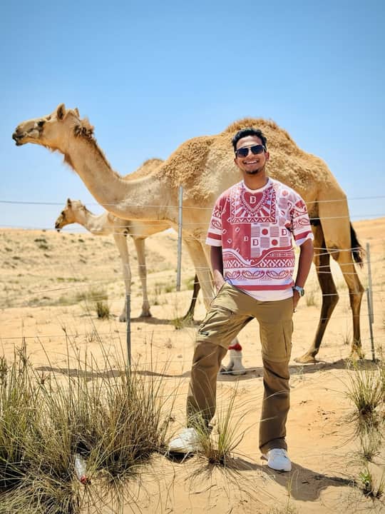 In desert grass with two camels behind, Dubai.