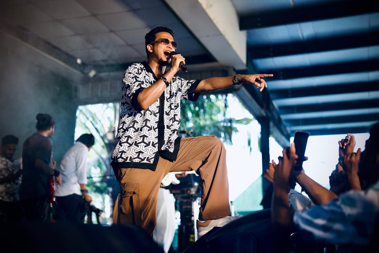 Tasrif Khan singing into a microphone under stage lights.