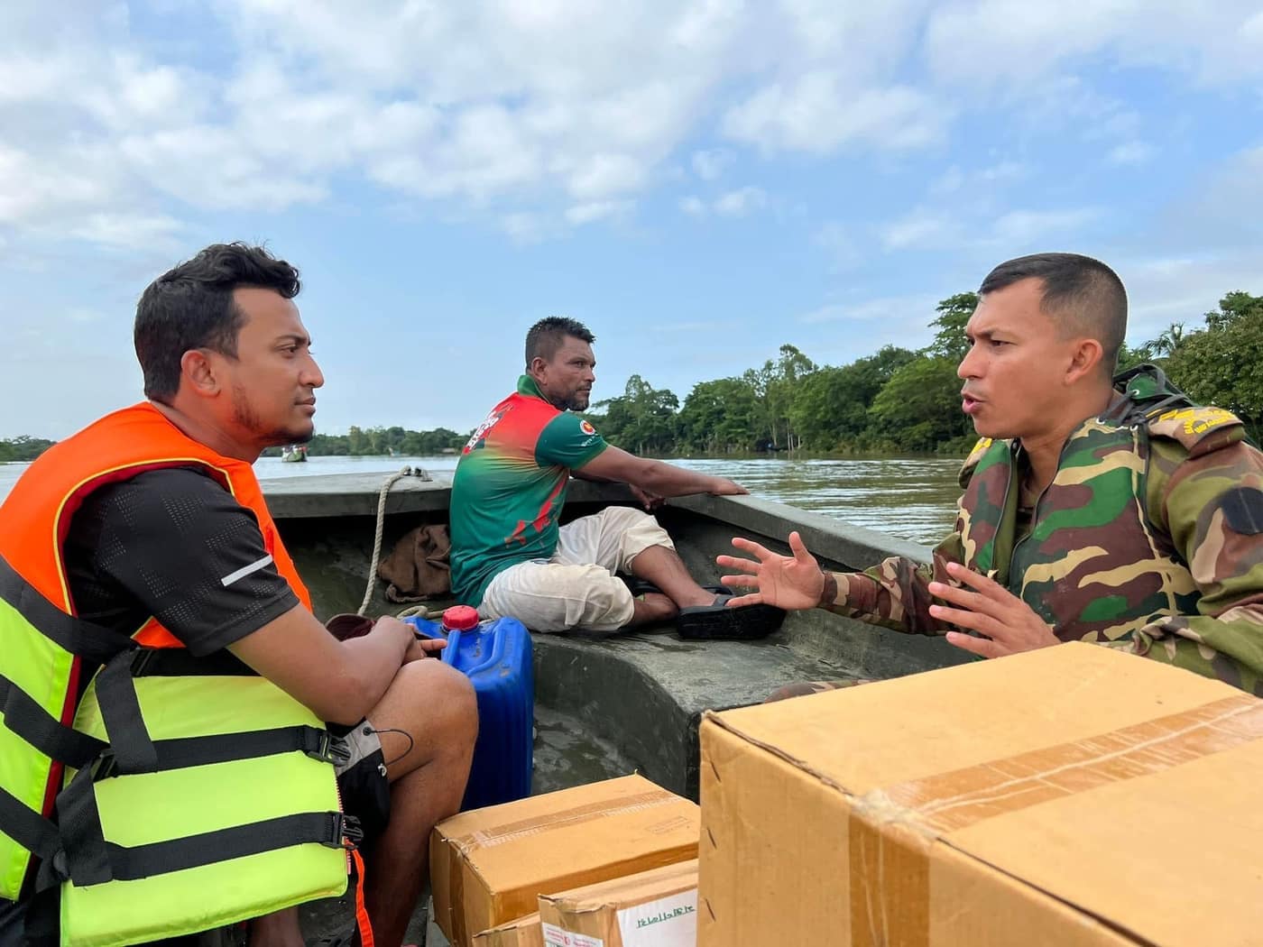Tasrif beside relief supplies on a boat, talking with a person in uniform.