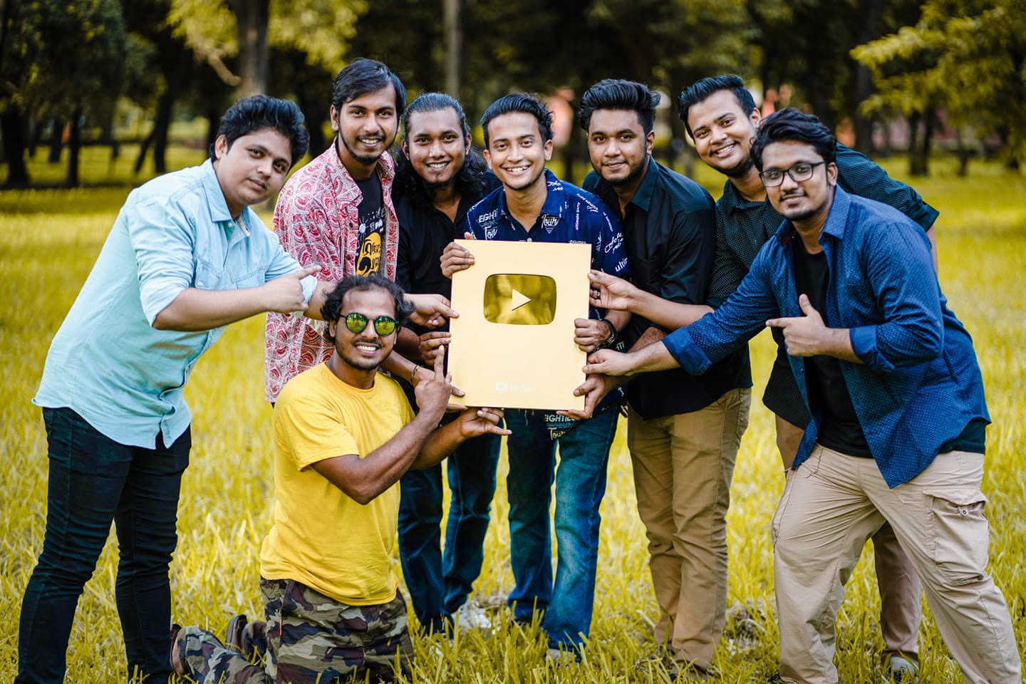 Eight people on a sunlit lawn holding Kureghor's gold YouTube play button.