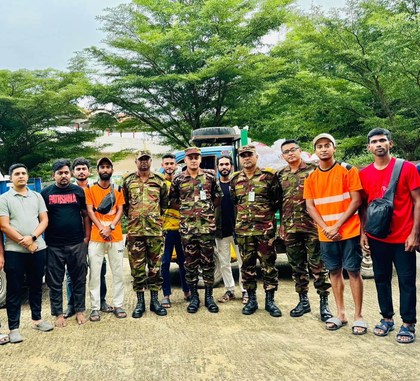A group standing in front of a loaded truck, some in high-visibility vests, some in camouflage uniform.