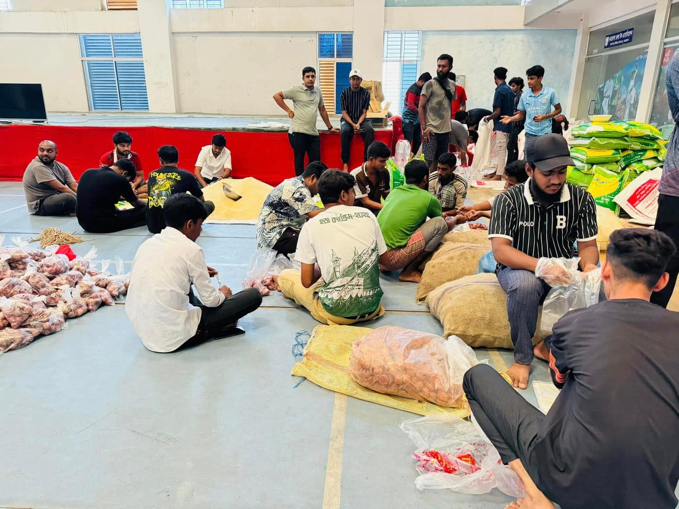 Volunteers sitting on a hall floor among rice sacks and loose onions, filling bags.