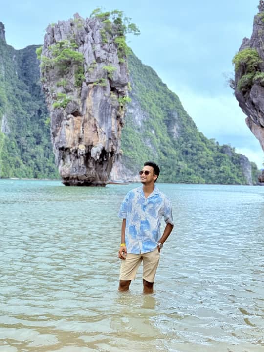 Standing in shallow turquoise water below a limestone karst, Thailand.