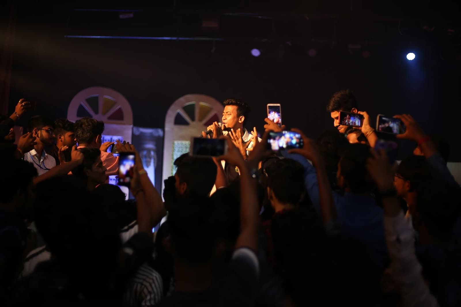 A crowd lit from the stage, arms and phones raised.