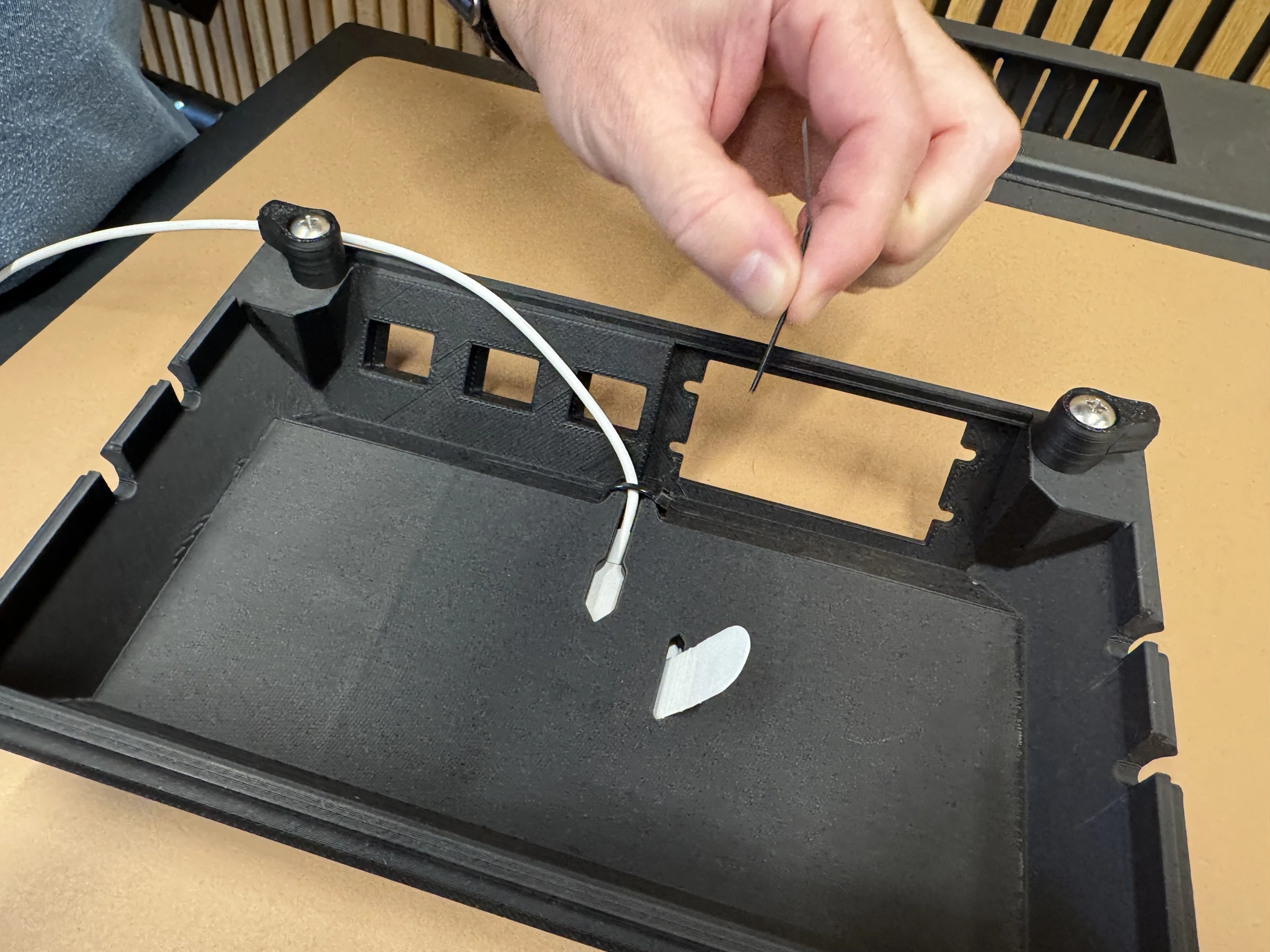 Photograph 16. Holding the trimmed cable-tie tail above the charging cable, which is tied to the underside of the insert.