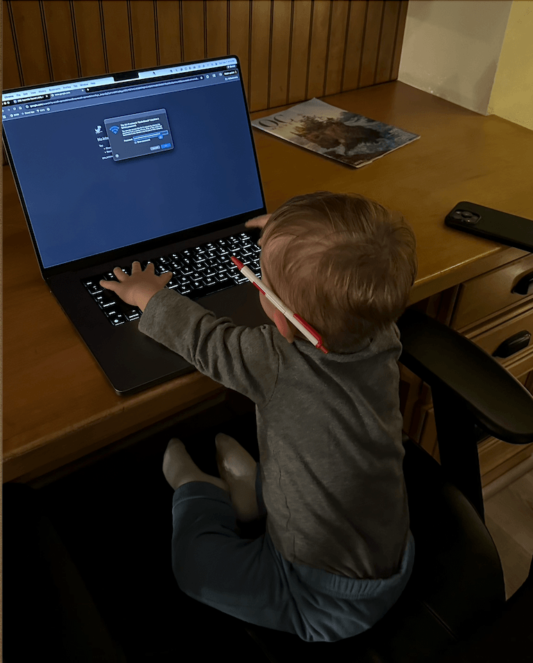 A toddler sitting at a desk with a laptop showing a Wi-Fi password prompt