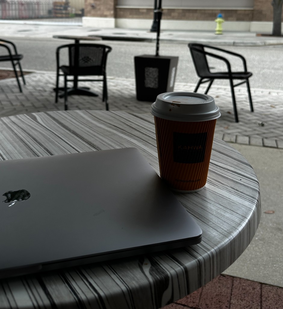 A closed laptop and Kahwa Coffee cup on an outdoor cafe table