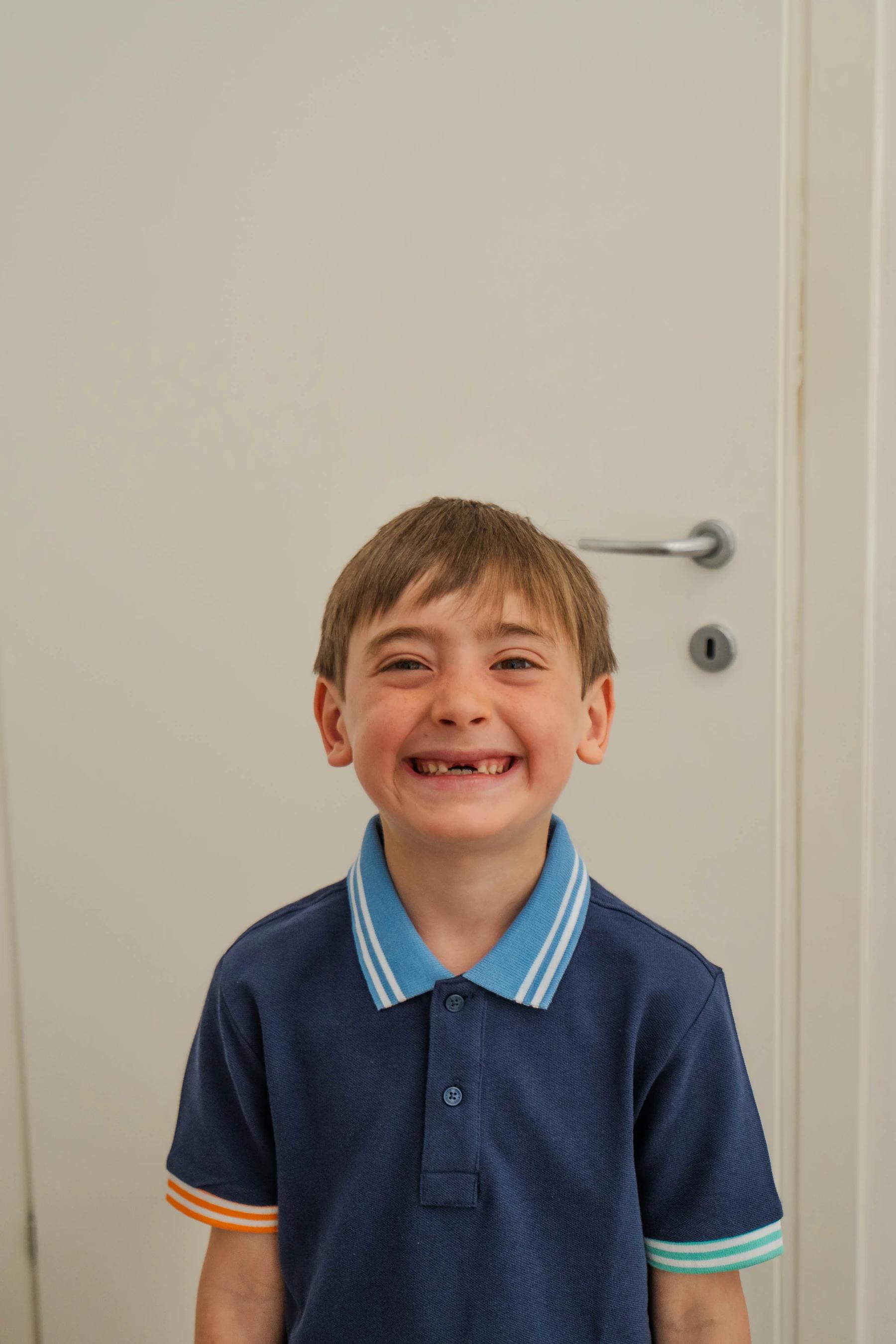 Bambino sorridente con polo blu navy e dente caduto, ritratto in primo piano nello studio di logopedia di Viterbo