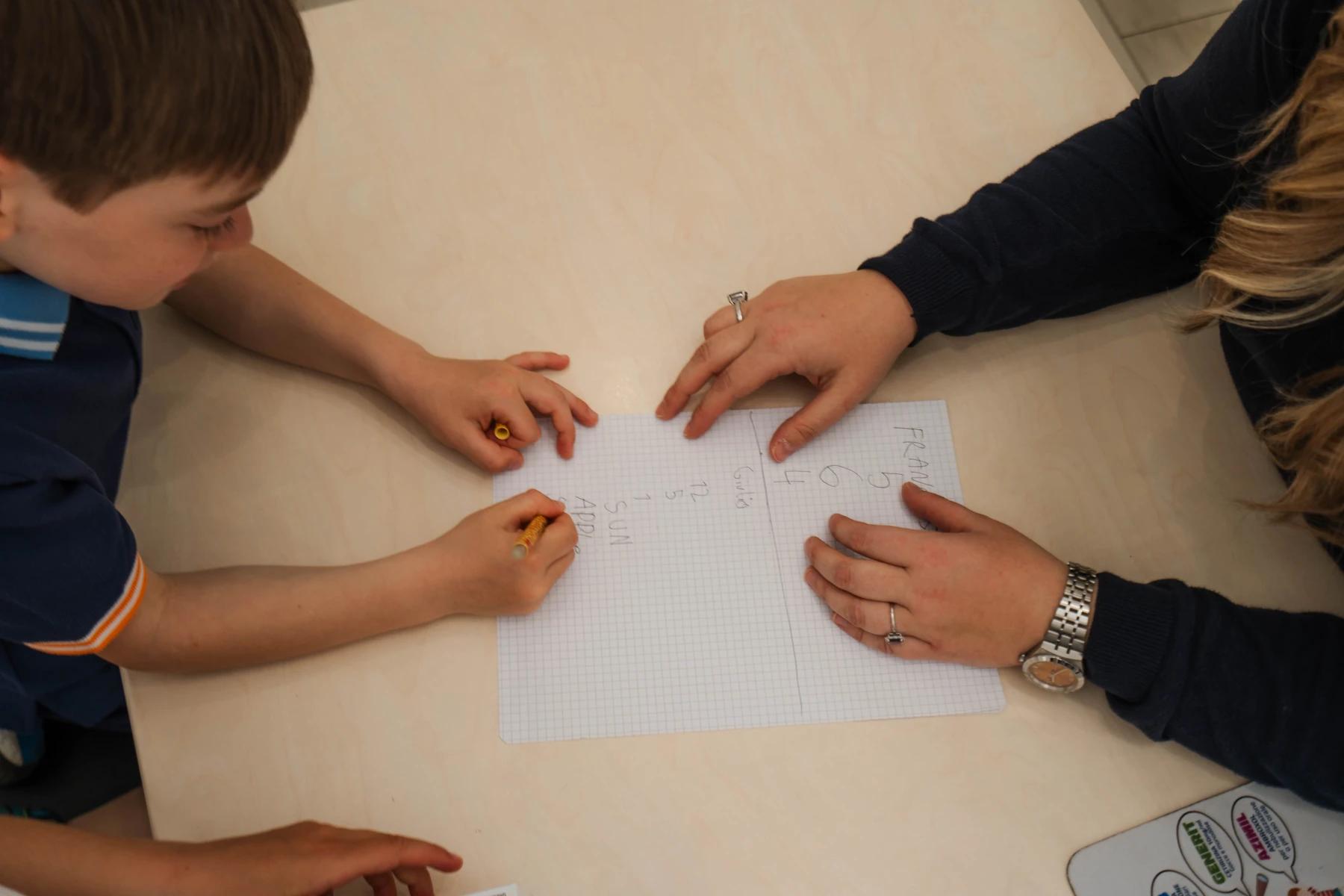 Mani di Mary che indicano un quaderno a un bambino durante la seduta di logopedia a Viterbo