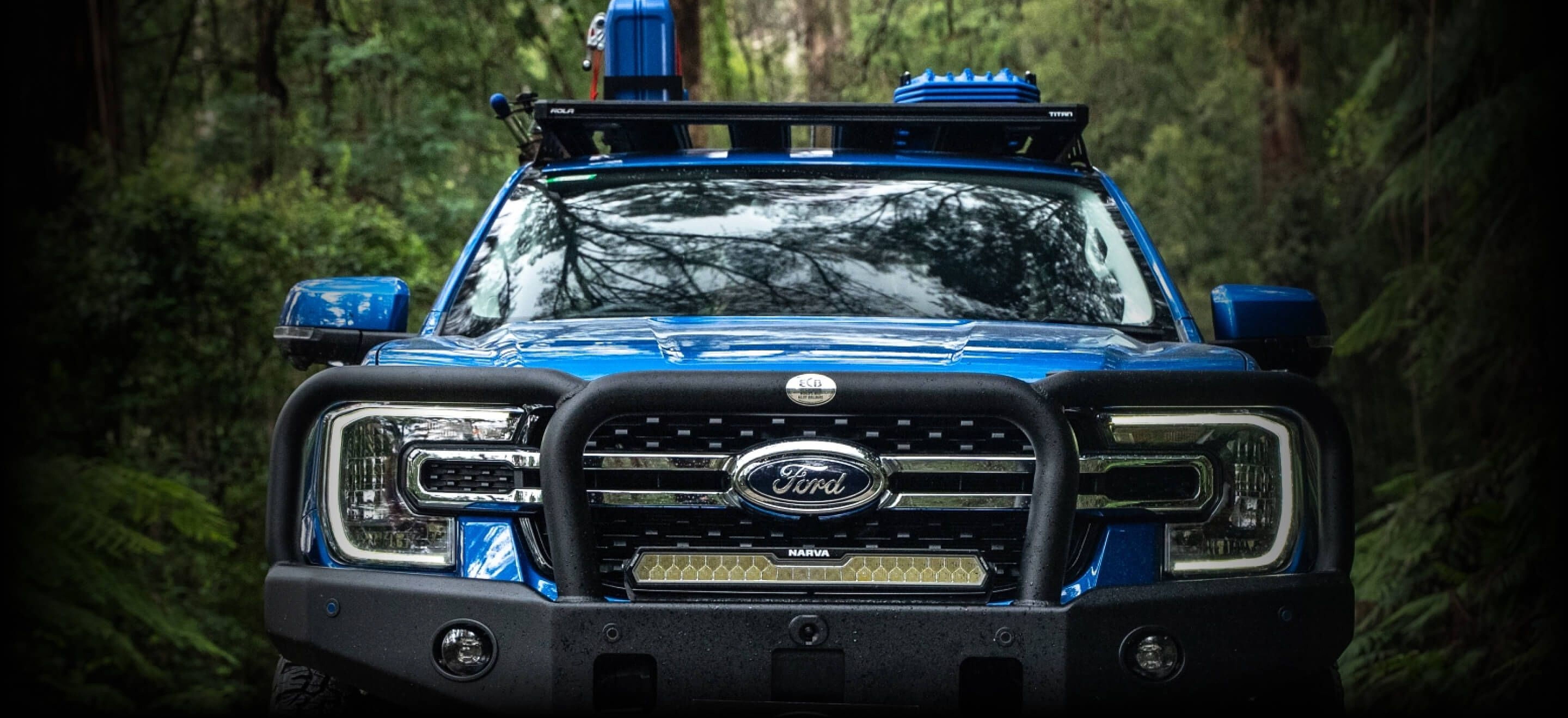 Blue Ford 4WD fitted with Narva driving lights and a light bar on a forest track