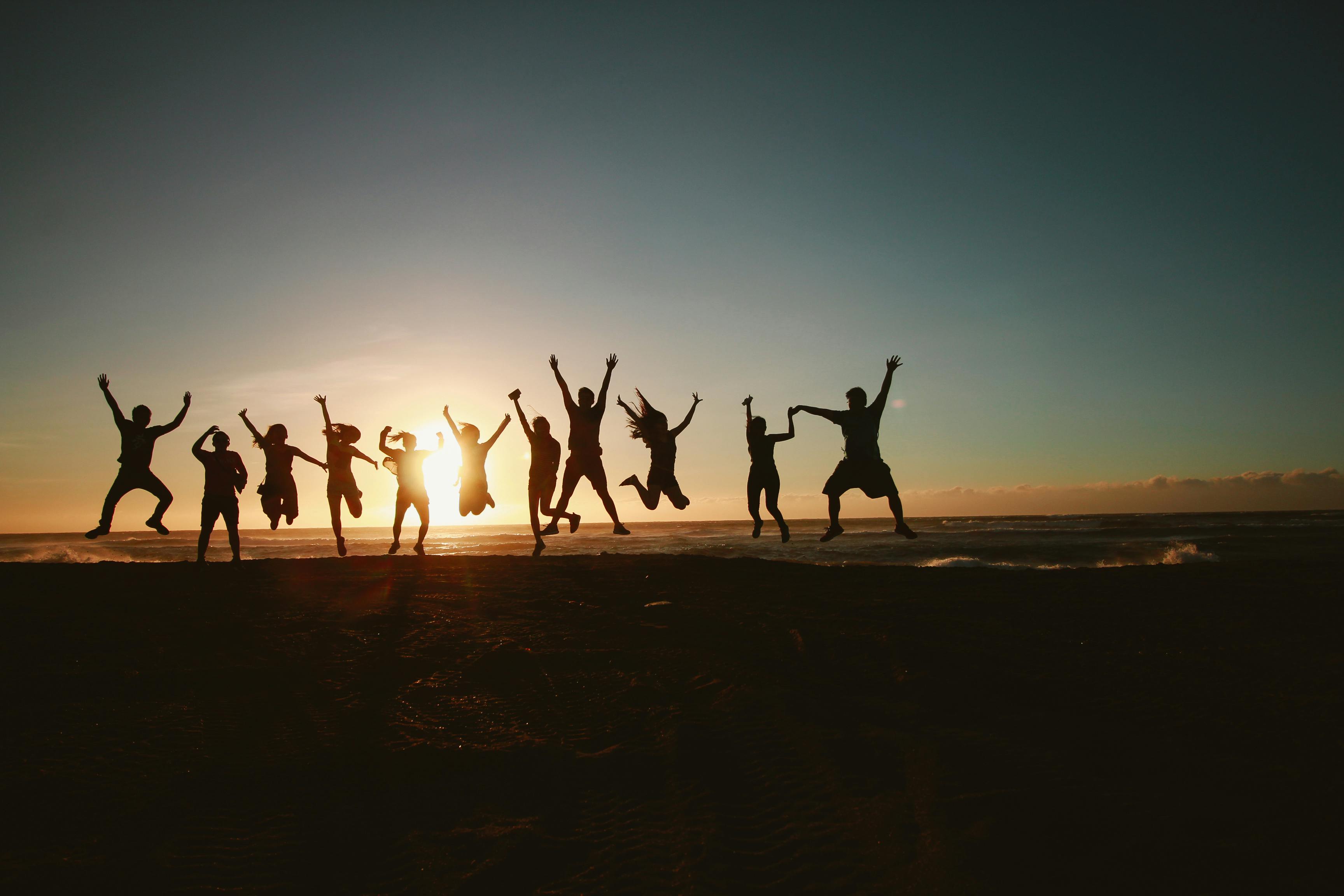 A group of people on the beach jumping excitedly.