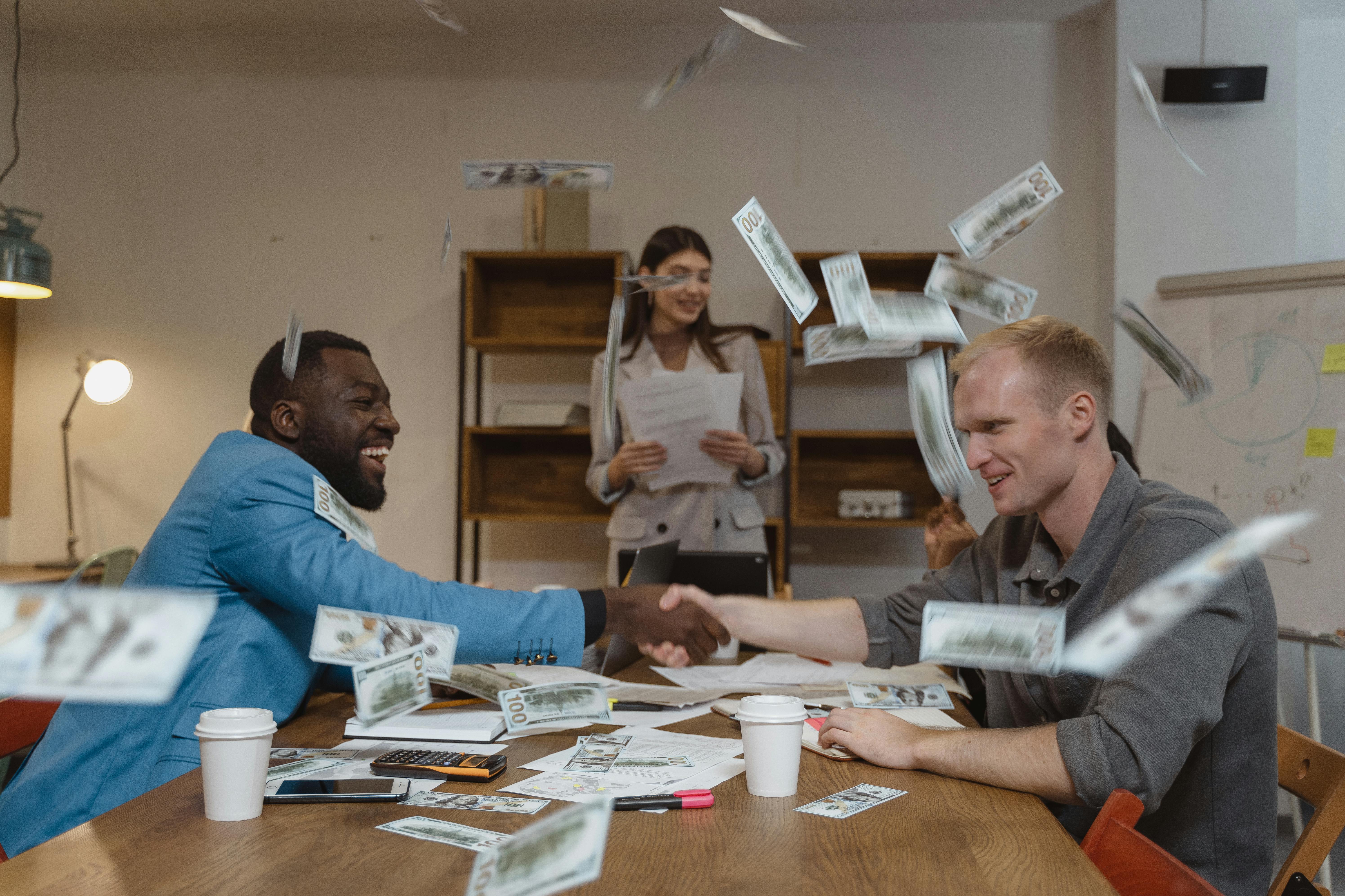 Two people shaking hands with money in the air.