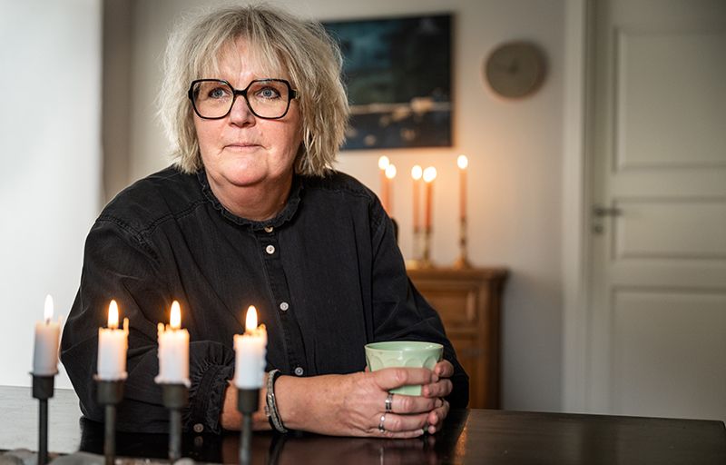 Helena Efraimsson sitter vid ett bord med en grön kopp i händerna. Stearinljus är tända framför och bakom henne.