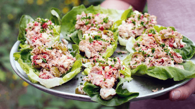 Tonfisksallad i salladsblad på ett silvrigt serveringsfat. En person håller i fatet.