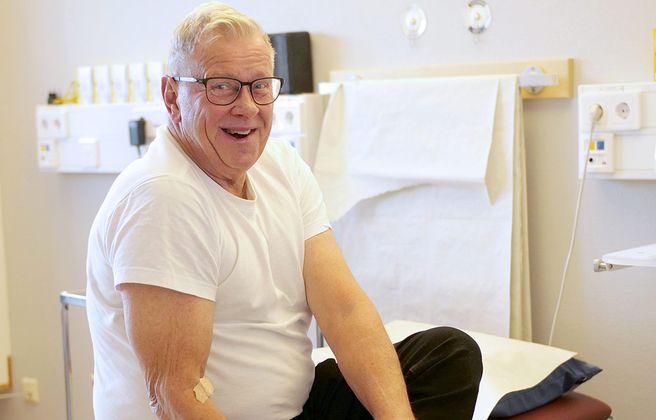 Glad man sitter på sjukhussäng.