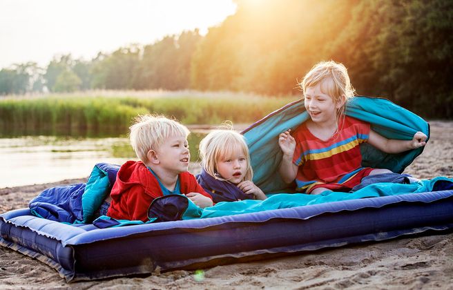 Barn ligger på luftmadrass på en strand och skrattar