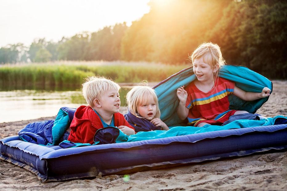 Barn ligger på luftmadrass på en strand och skrattar