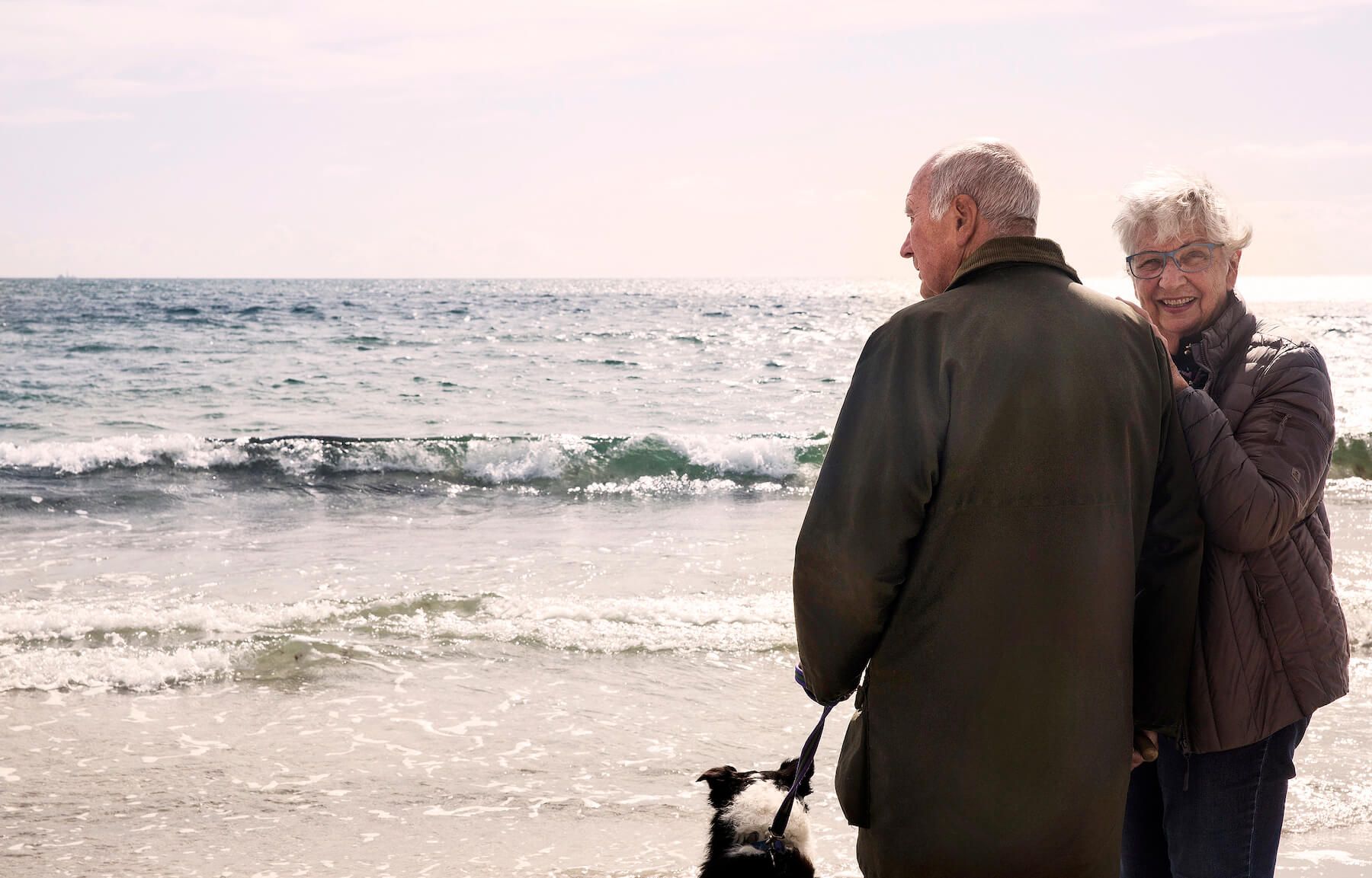 Äldre par med hund på strandpromenad vid havet