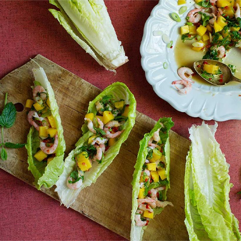 Räksallad med mango i sallatsblad på en skärbräda.