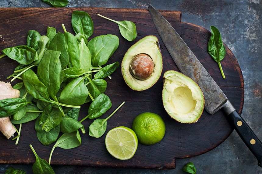 Bladspenat, avokado och en lime ligger på en skärbräda av trä