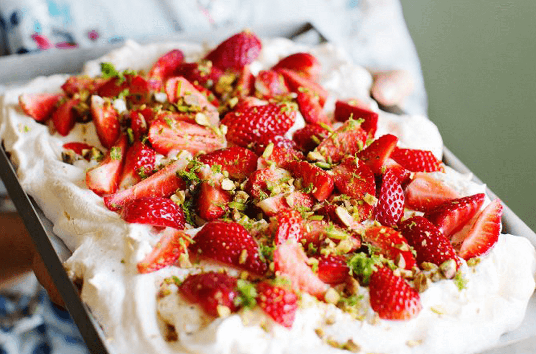 Pavlova-tårta med jordgubbar och hackade pistagenötter ovanpå.
