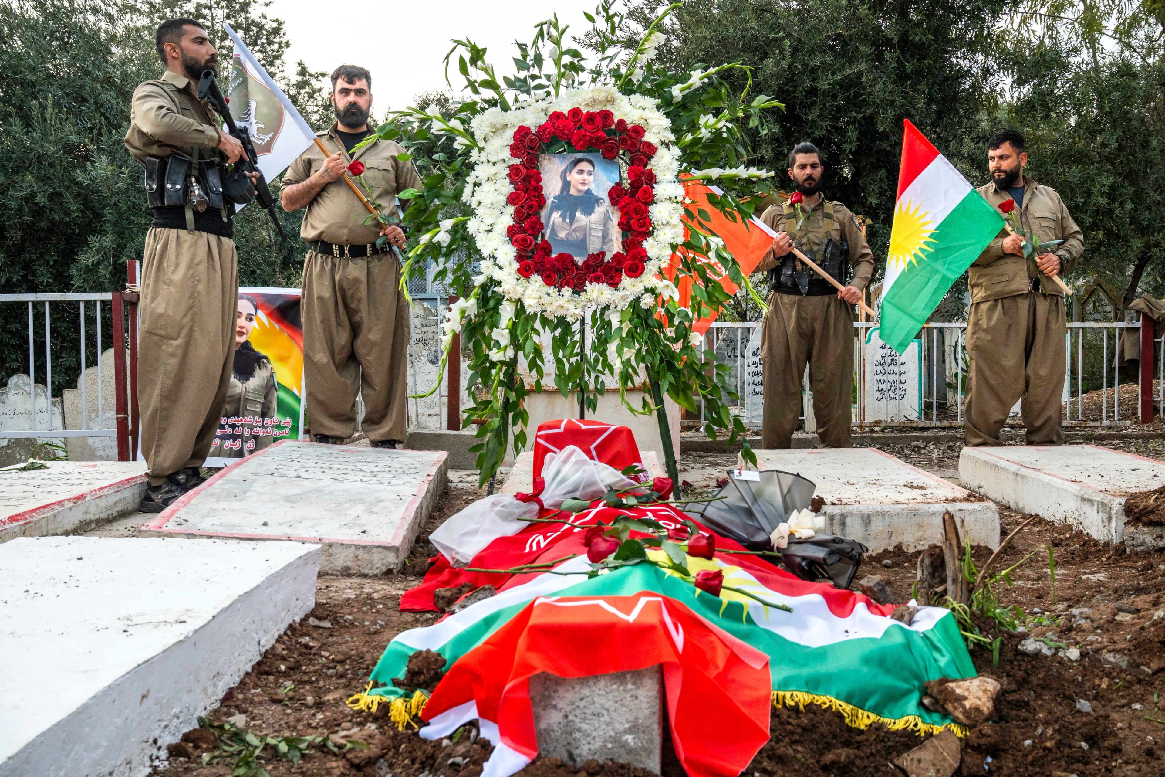 The grave of Ghazal Molan, draped in the Kurdish flag, the Komala star, and red roses, surrounded by fellow soldiers at her burial in Sulaymaniyah, Iraq. 