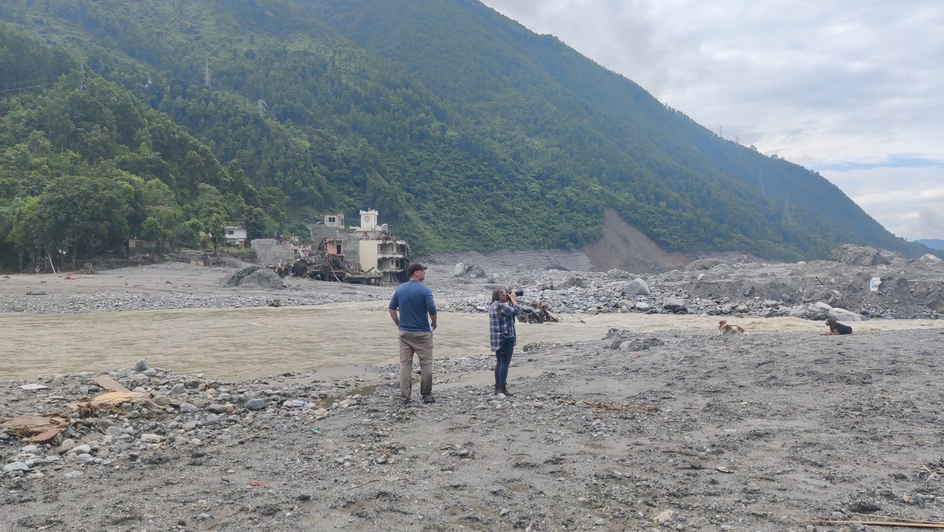 A flood-ravaged stretch along the Trishuli River in Rasuwa district, Nepal, shows extensive deposits of mud, rocks and debris, with damaged structures visible in the background. Photo: Yogesh Nepal