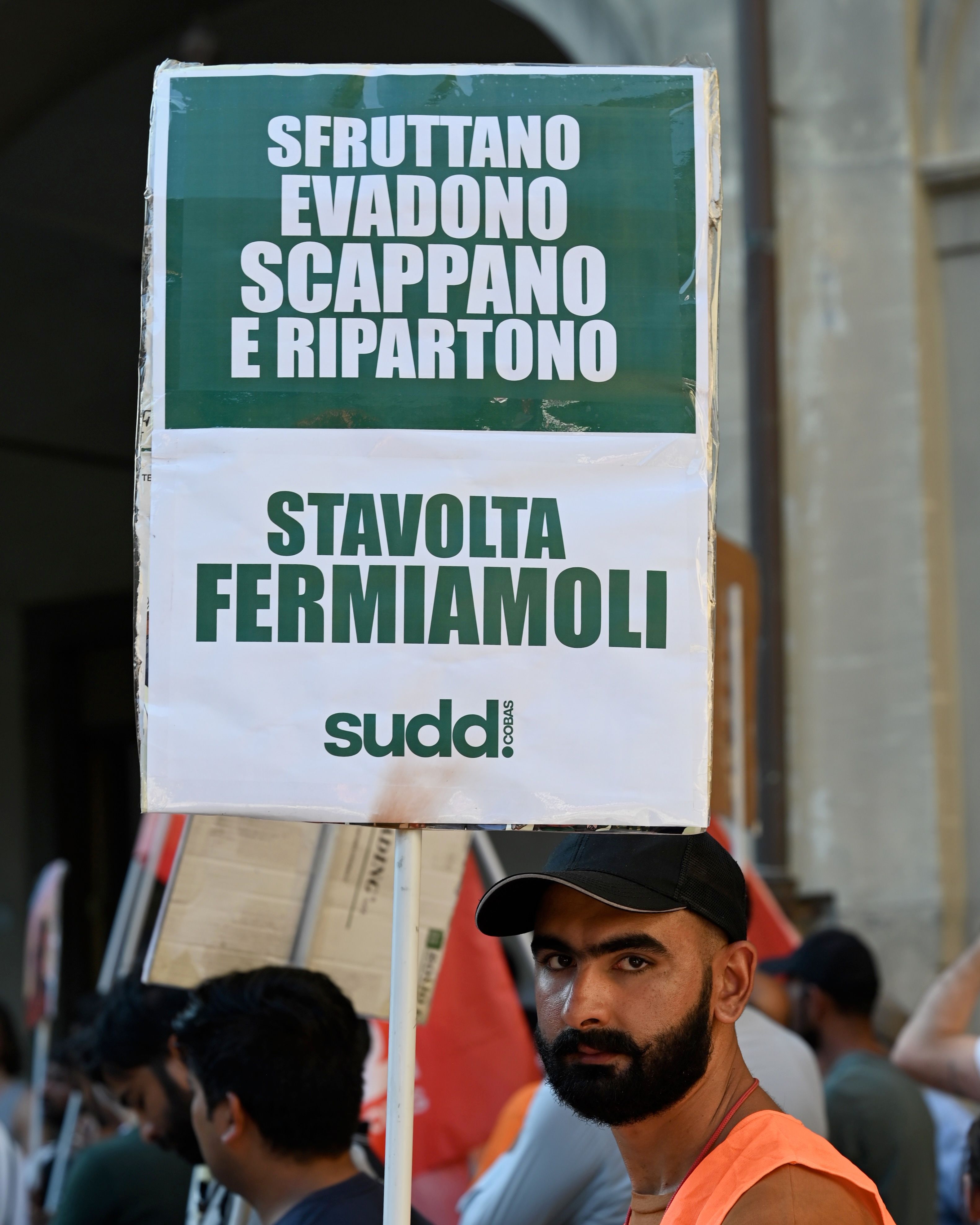 One of the migrant workers holds a placard reading “They exploit us, evade taxes, escape and redistribute,” along with the slogan “Enough, let’s stop them,” during a march organised by Sudd Cobas in Prato, Italy, on July 6, 2026. Photo: Special Arrangement/Sudd Cobas