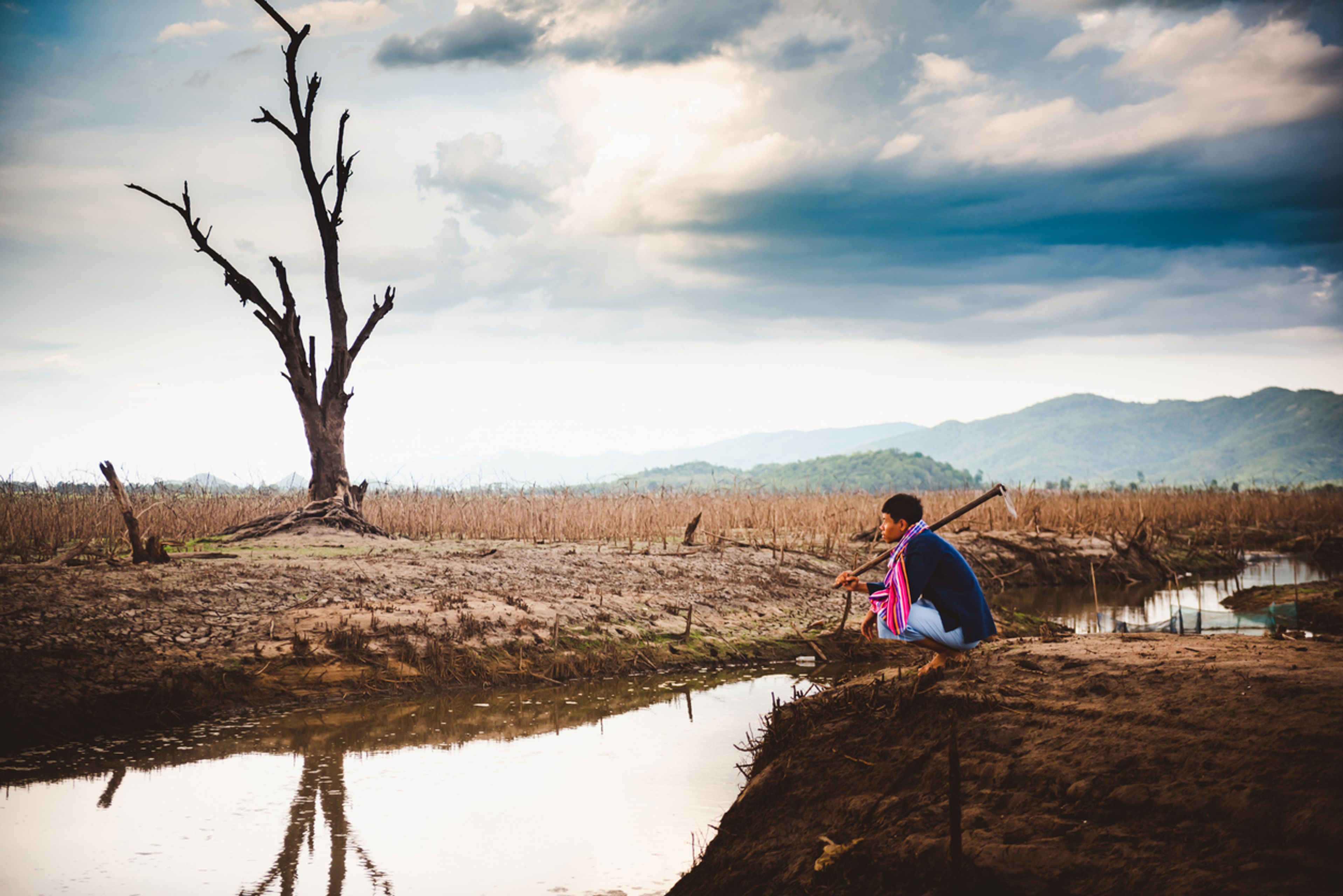 A Myanmar farmer sits on cracked, parched earth beside a drying water body. The UN says El Niño is expected to leave 49 million more people food insecure by the end of 2027. Photo: iStock