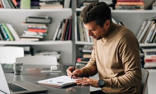 Man sitting at desk, writing on a notepad