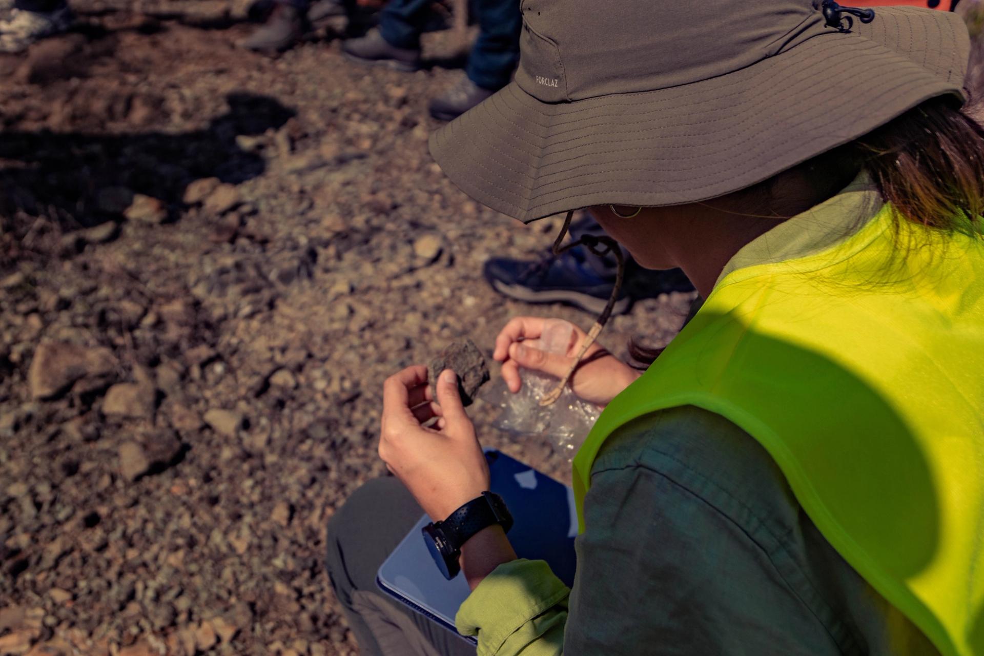 GSA Cuba trip attendee in yellow vest in field examining a rock