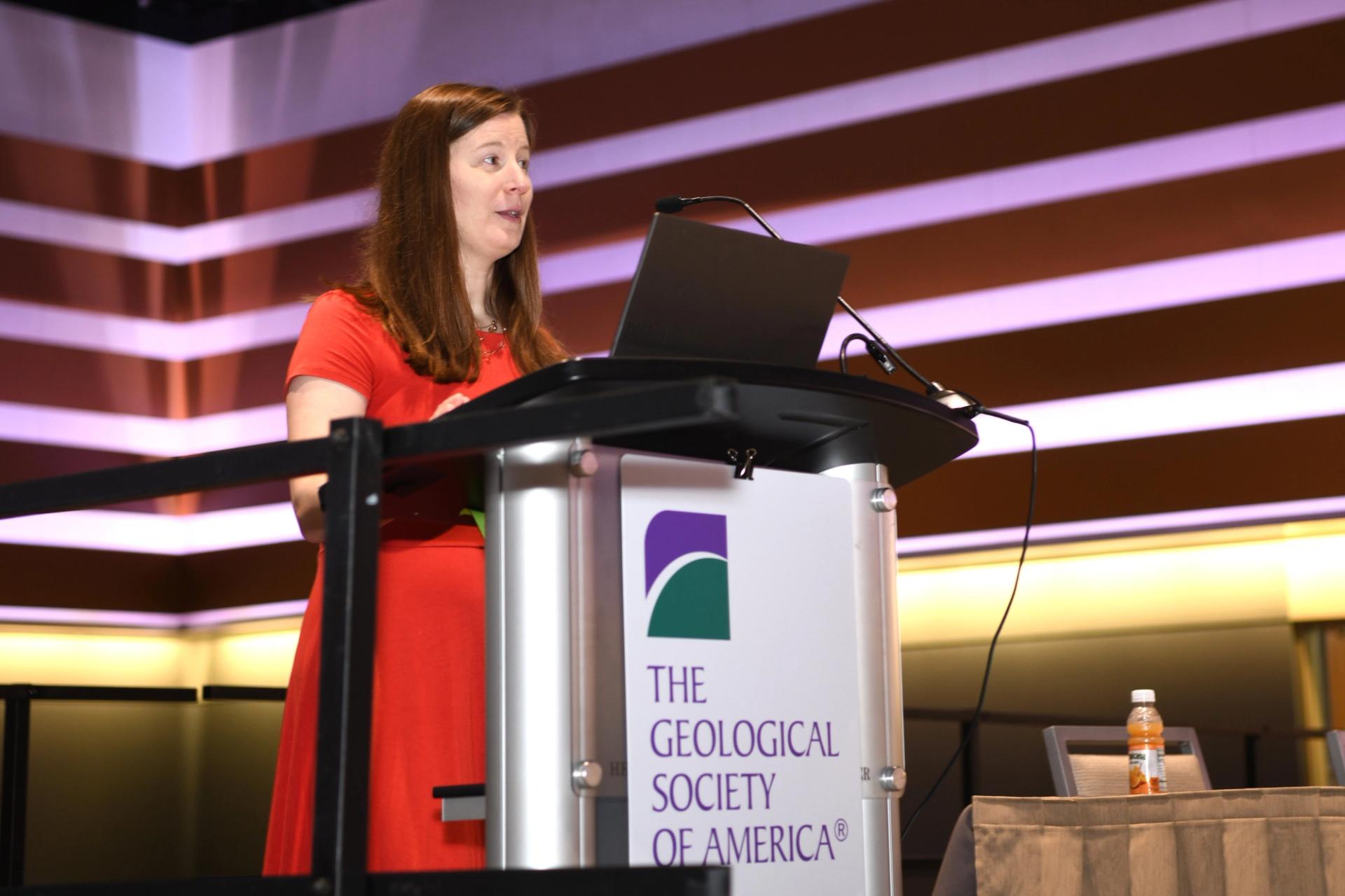 GSA Connects attendee giving presentation while standing behind a microphone stand with the GSA logo on the front in large meeting room