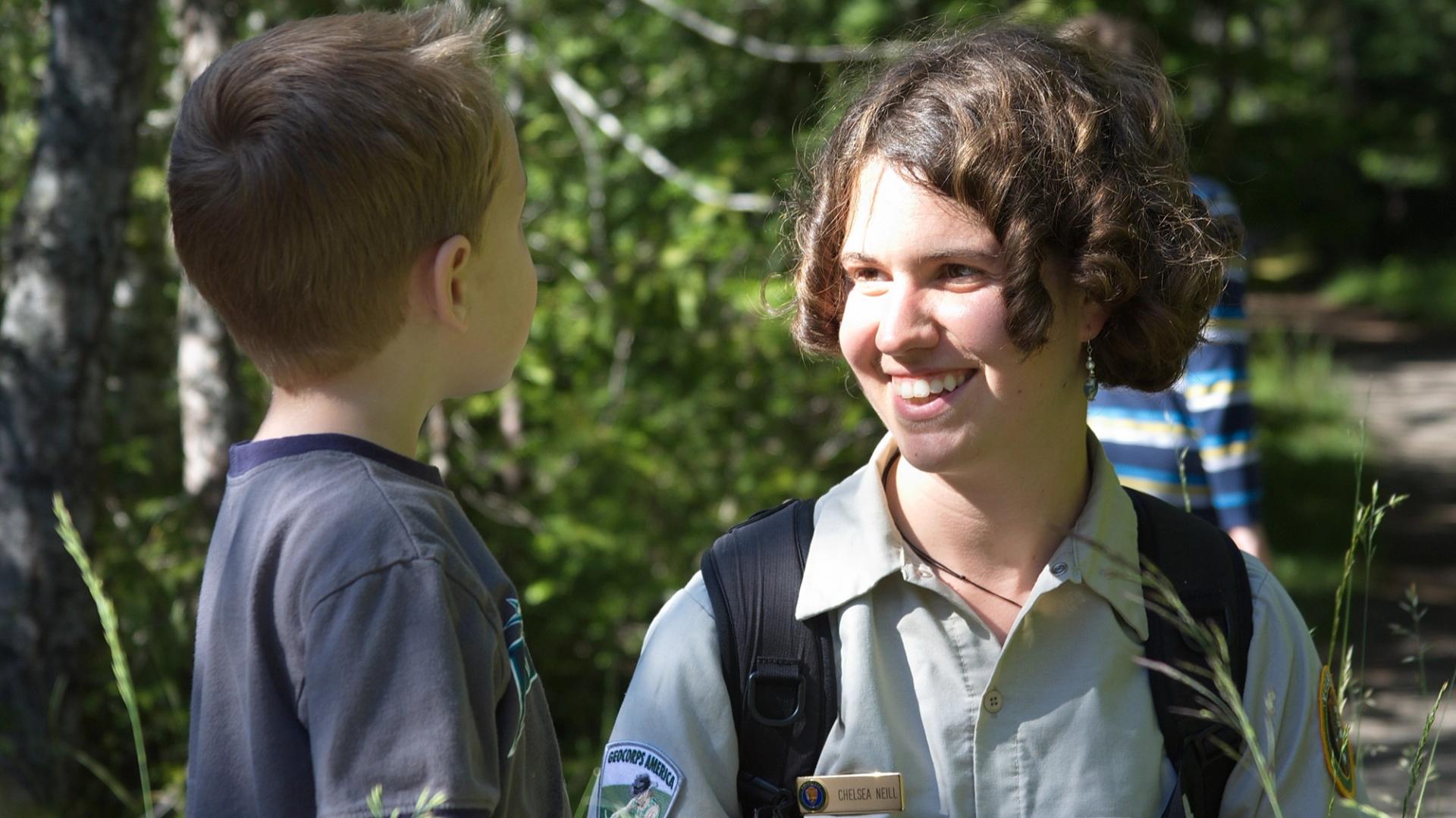 GeoCorps participant in the field smiling while talking to a young kid