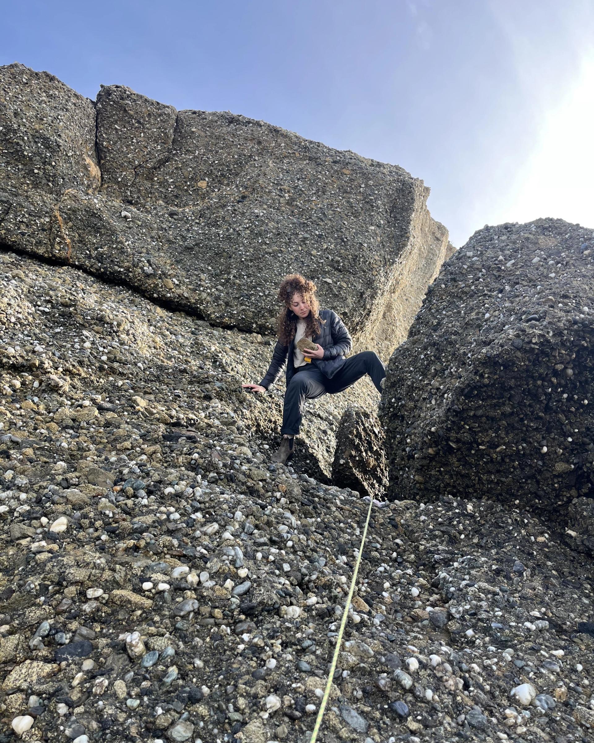 Photo of GSA graduate student research grant recipient conducting geoscience research in the field looking at rock while climbing a mountain