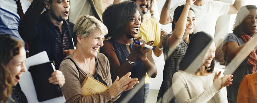 A diverse group of people smiling and clapping in a joyous celebration. The mood is cheerful, with a focus on unity and happiness.