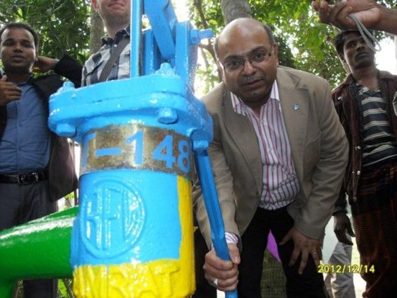 A man stands near a brightly colored manual water pump.