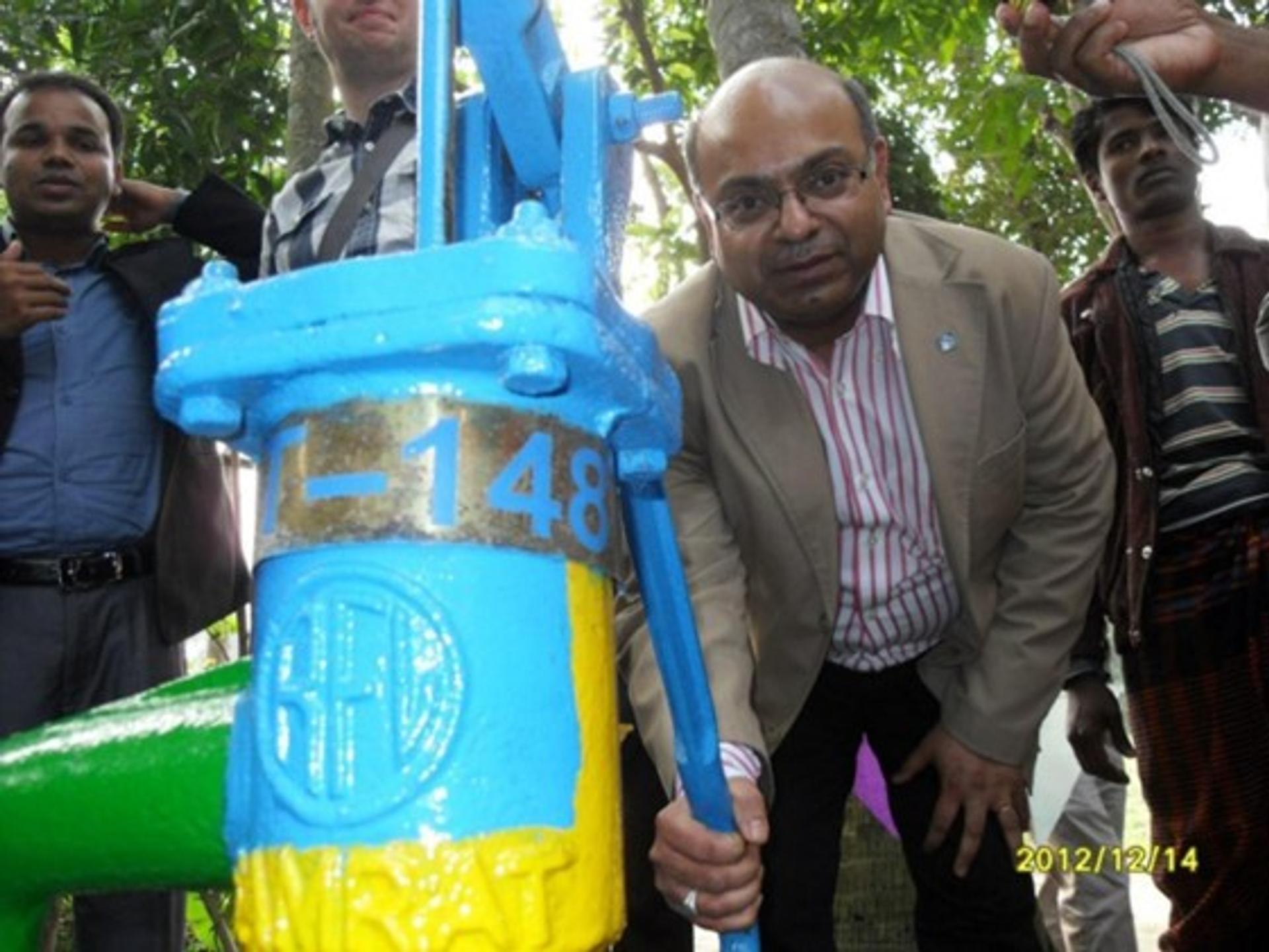 A man stands near a brightly colored manual water pump.