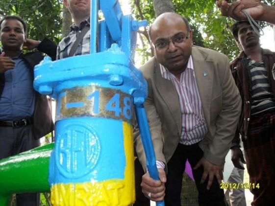 A man stands near a brightly colored manual water pump.