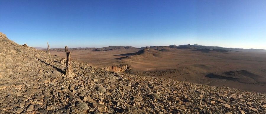 Rocks of various sizes cover the top of a hill that overlooks land and formations below.