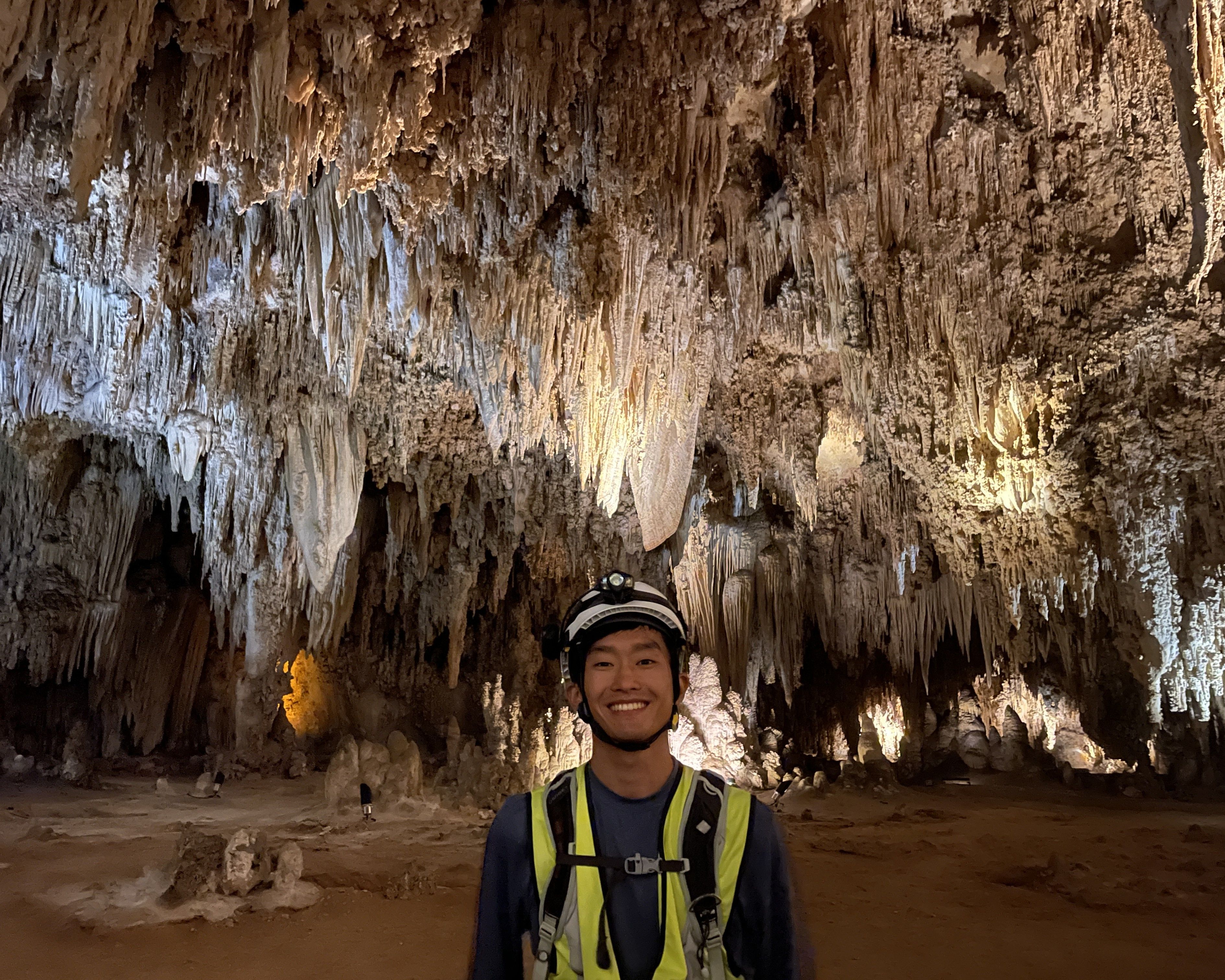 GeoCorps participant in cave with large stalactites hanging from ceiling in the background