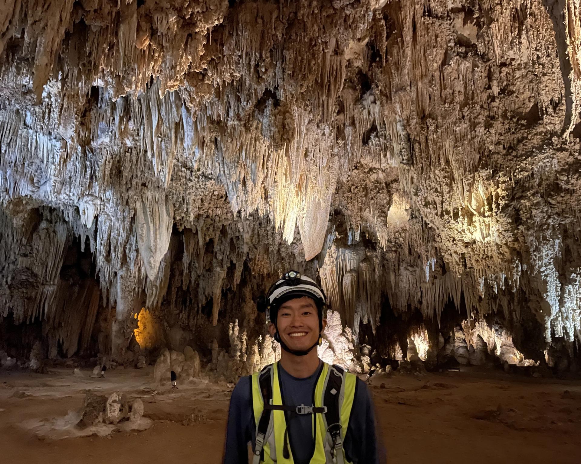 GeoCorps participant in cave with large stalactites hanging from ceiling in the background