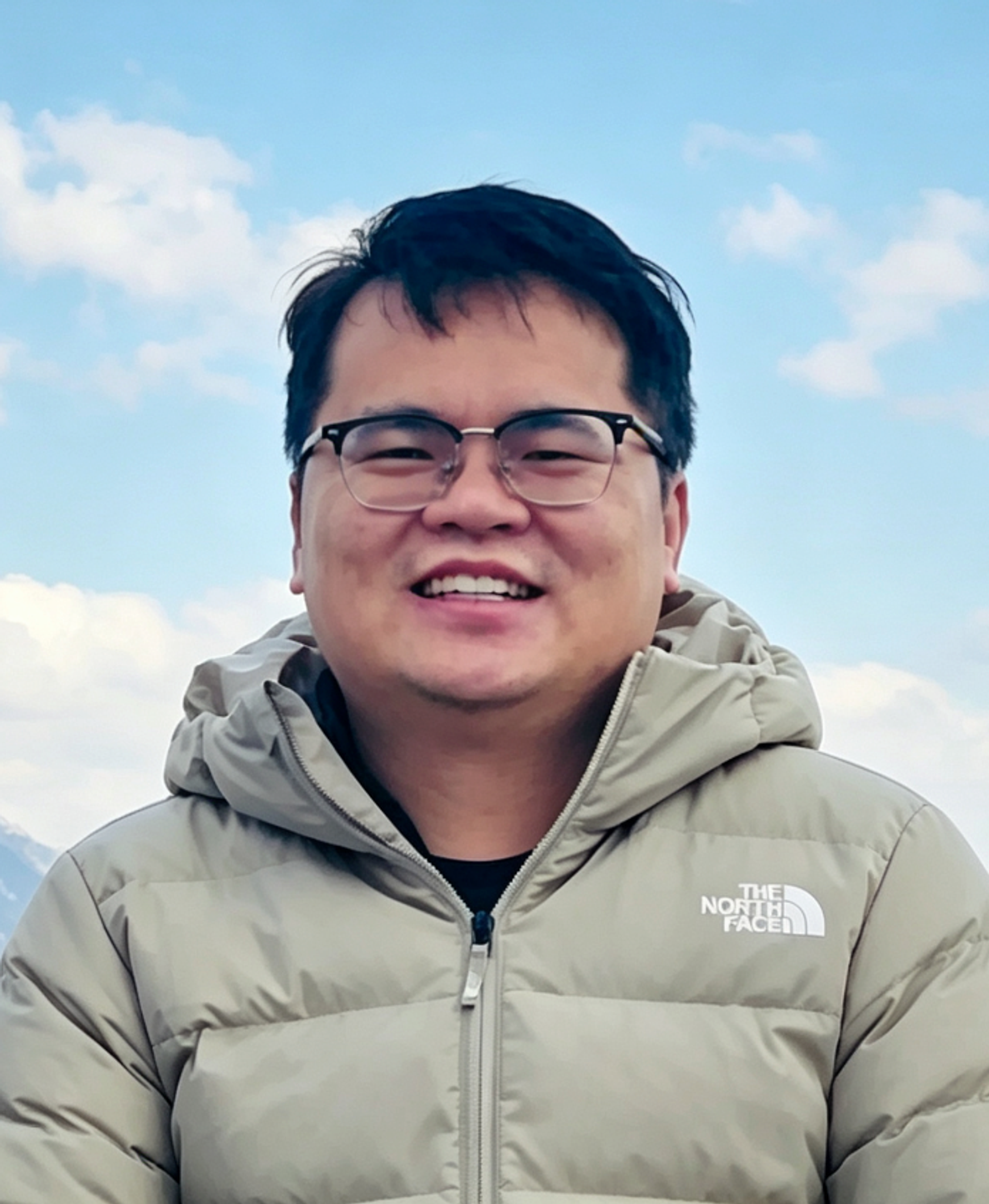 Yun-Chuan Zeng in a tan coat and glasses with a blue and white sky in the background.