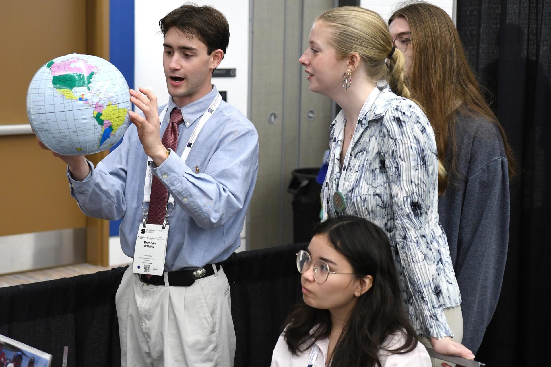 A young man enthusiastically shows a globe to three attentive young women. They're engaged, suggesting a dynamic, educational setting.