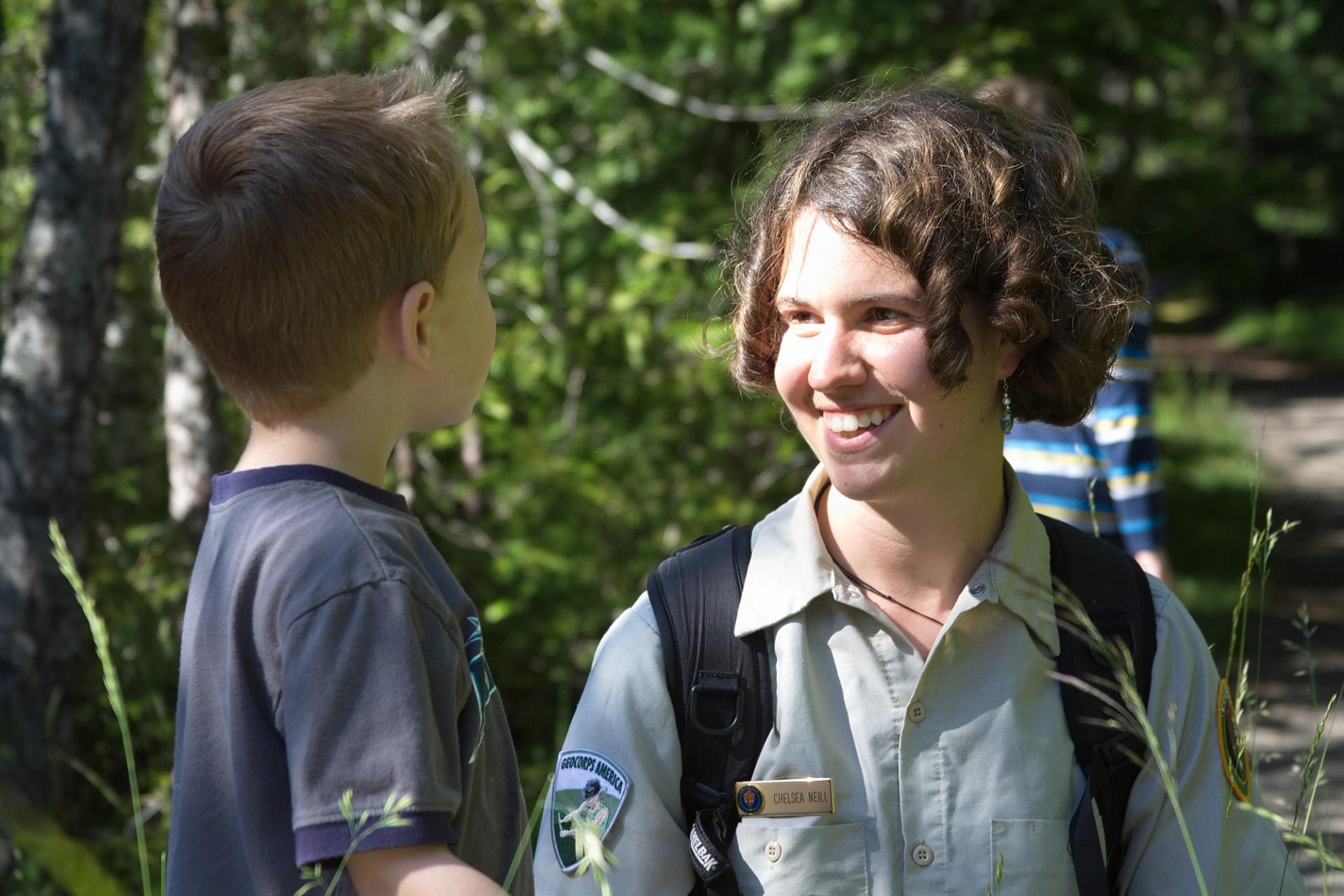 Photo of GeoCorps Participant in the field smiling while talking to little kid