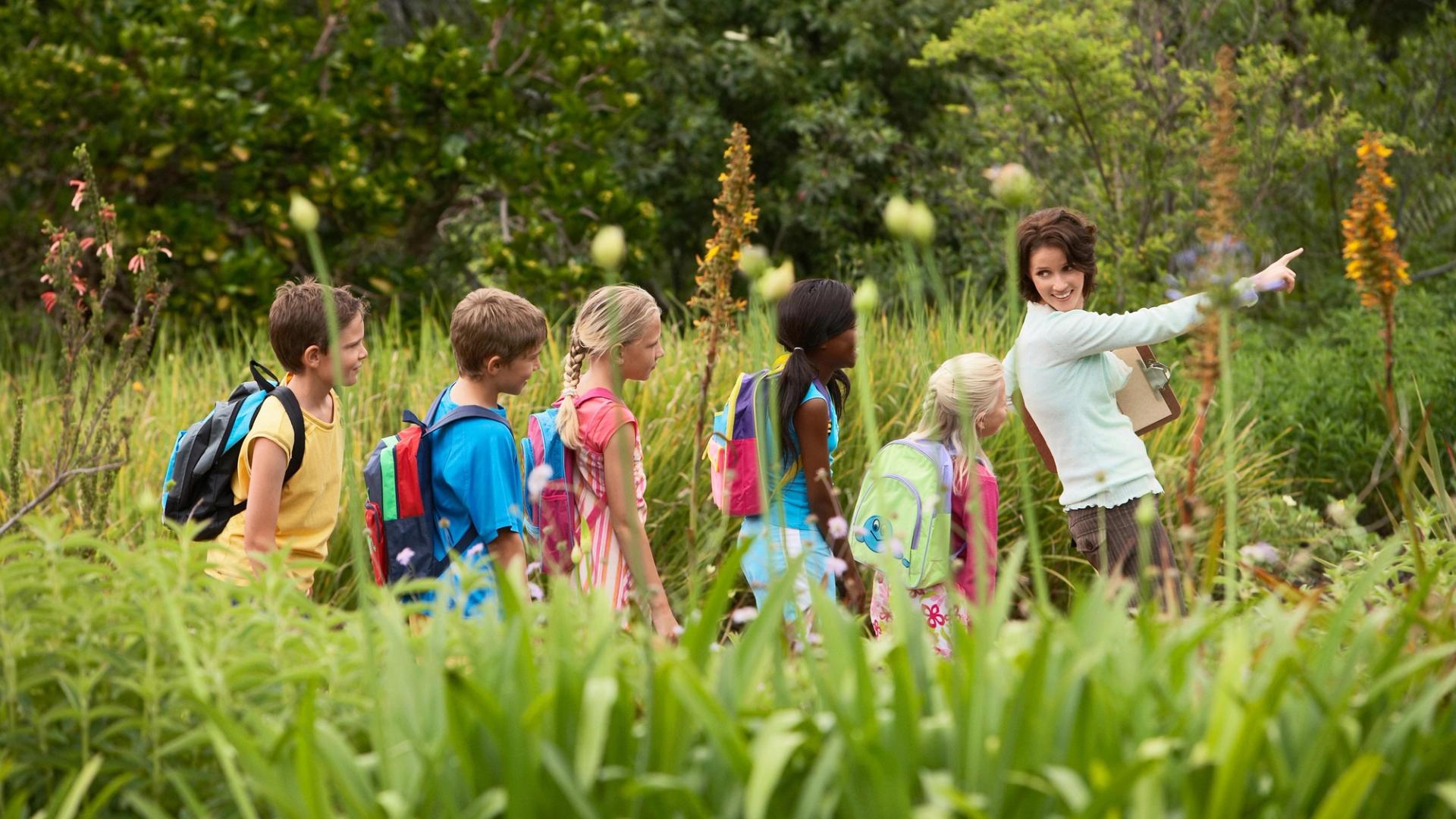 Teacher leading students on outdoor adventure through tall grass