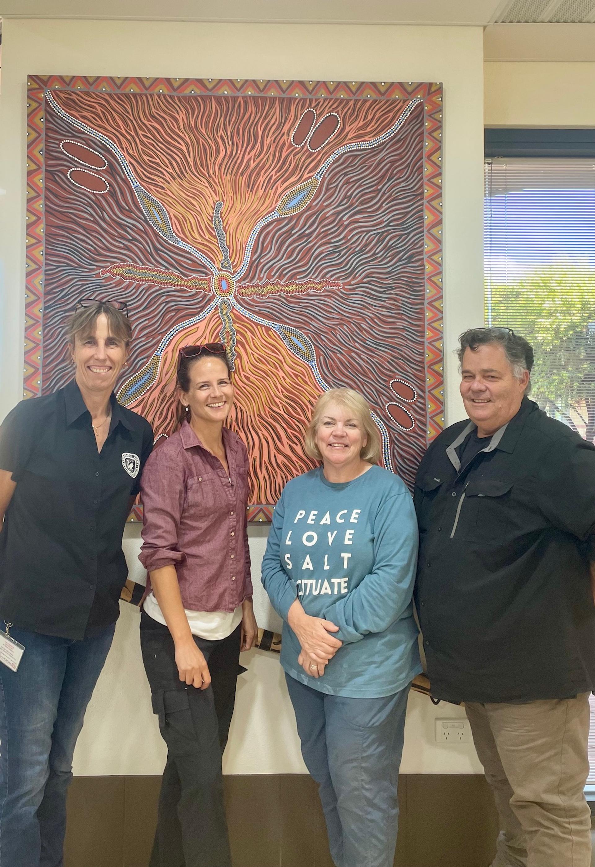 Four adults smile in front of an orange and maroon painting.