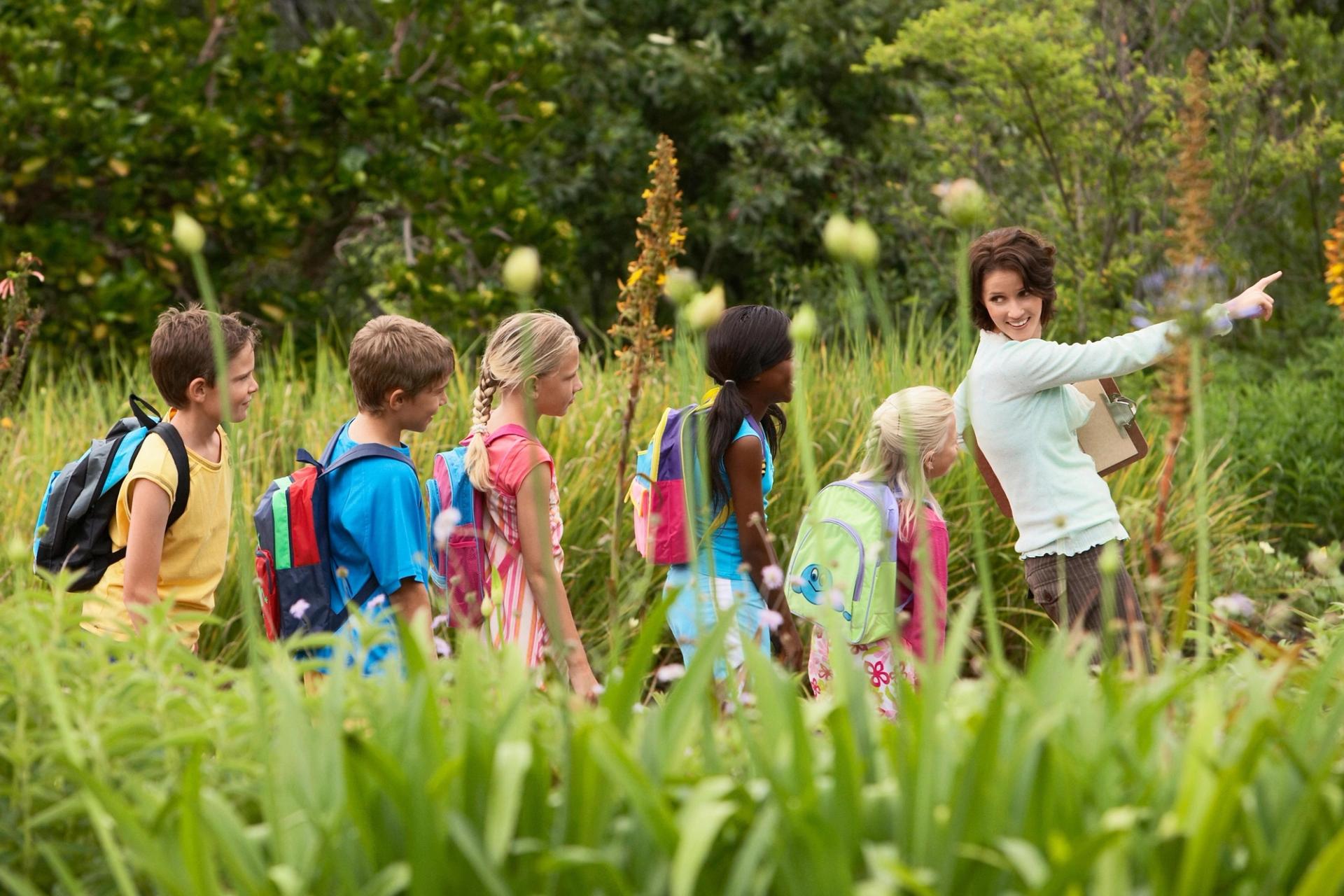 Teacher leading students on outdoor adventure through tall grass