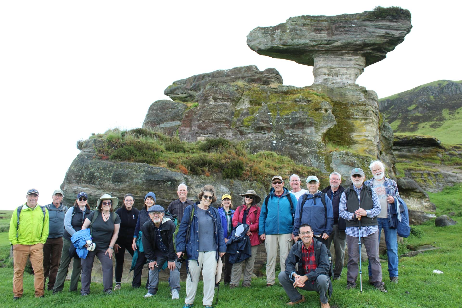 A group of geologists in outdoor gear smiling in front of a mossy rock formation.
